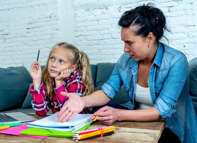 Mother becoming frustrated with daughter whilst doing homework sitting on sofa At home in learning difficulties homework parenting and education concept